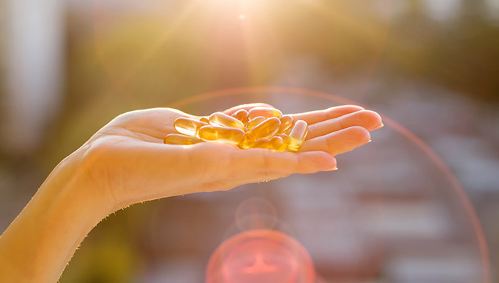 Vitamin D capsules in hand with lens flare in the background