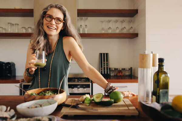 Middle age woman in her kitchen with healthy food and green smoothie drink