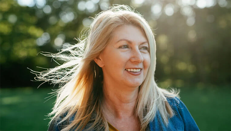 Mature caucasian woman outdoors with sunshine behind her highlighting her hair.